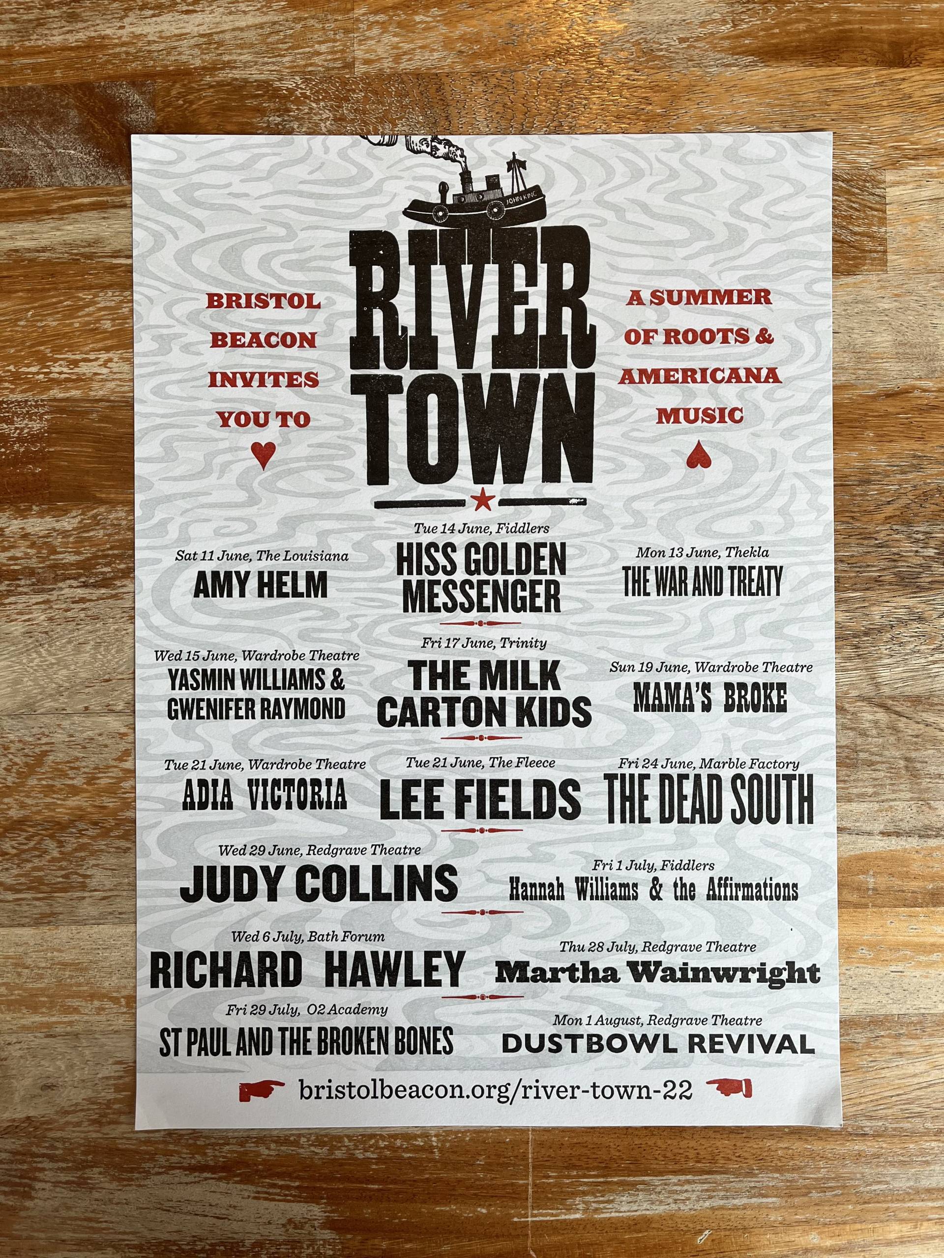 A letterpress printed poster for River Town 2022 displayed on a worn wooden surface. Text reads: Bristol Beacon invites you to River Town